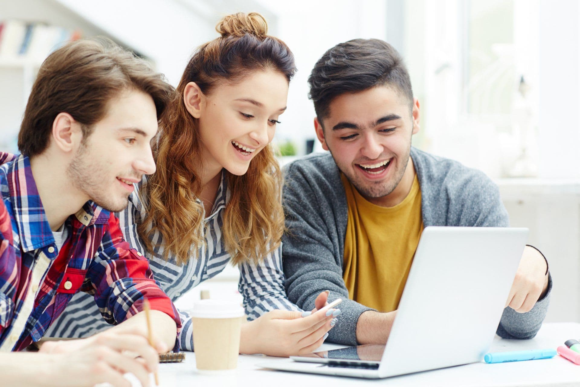 Tres estudiantes sonrientes trabajando juntos en una laptop